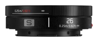 A black camera lens side view showing a focus ring with distance markings from 0.25m/0.82ft to infinity, a focal length of 26, and an S logo.