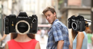 A man in a plaid shirt walks down a street, looking back at a woman with a Pentax K-1 Mark II camera for a head, while ignoring a woman with a vintage Pentax film camera for a head.