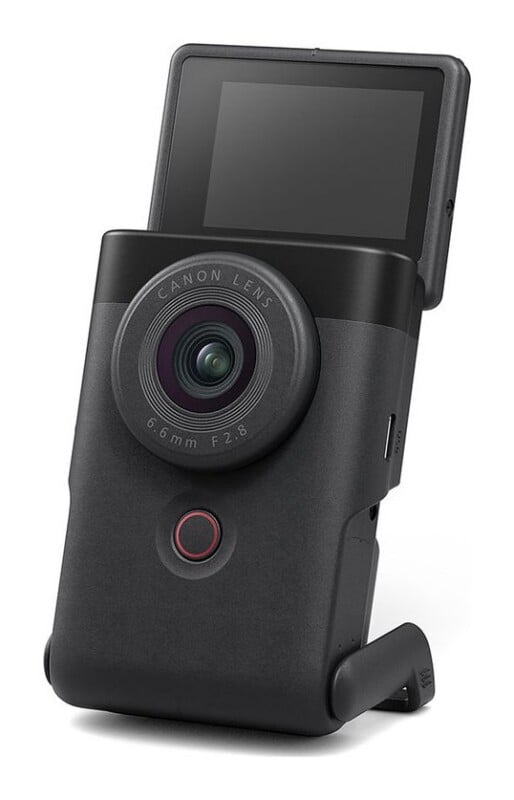 A black Canon PowerShot V10 vlogging camera stands upright on a white background with its screen flipped up.