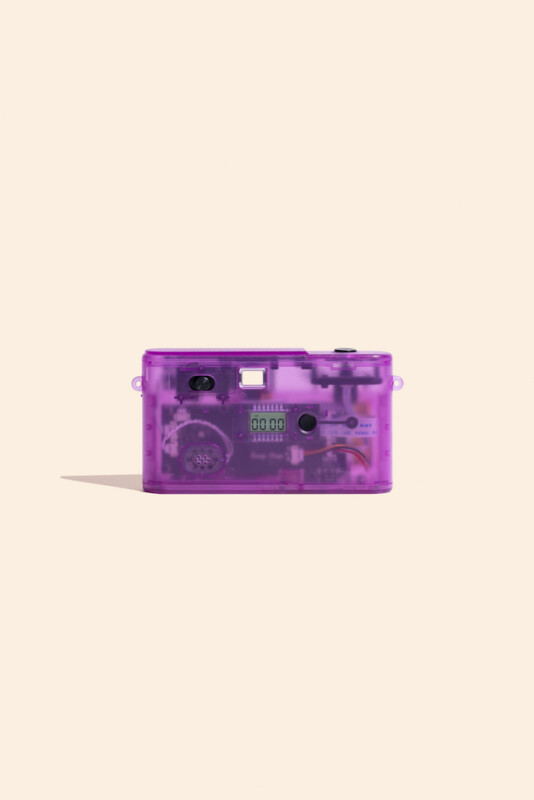A translucent purple digital camera with a visible internal circuit board and a small LCD screen displaying "00 00" sits against a light beige background.