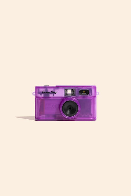 A purple, translucent digital camera with the text "Camp Snap" on the front, centered against a light beige background.