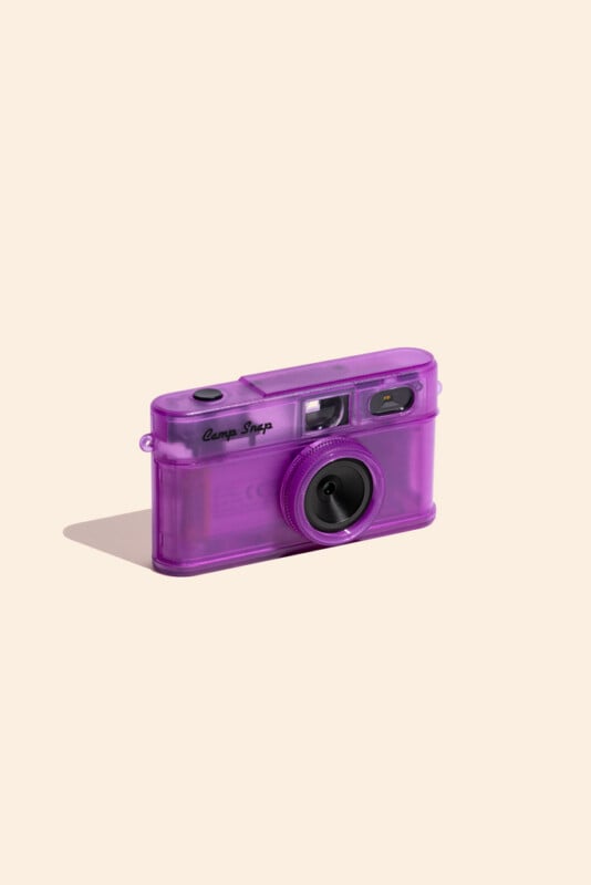 A purple, translucent digital camera with the text "Camp Snap" on the front, positioned at an angle on a light beige background.