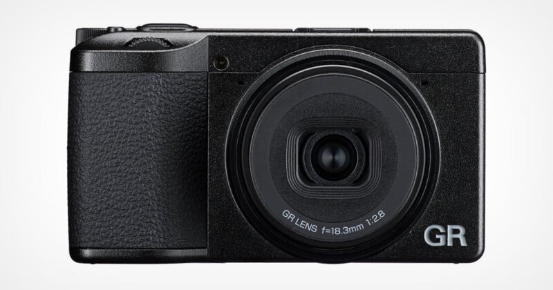 A front-facing view of a black compact digital camera with a prominent lens barrel labeled "GR LENS f=18.3mm 1:2.8" and "GR" branding.