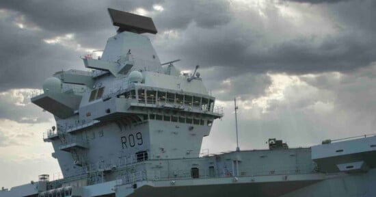 The island superstructure of a grey aircraft carrier marked with the pennant number R09 under a cloudy sky.