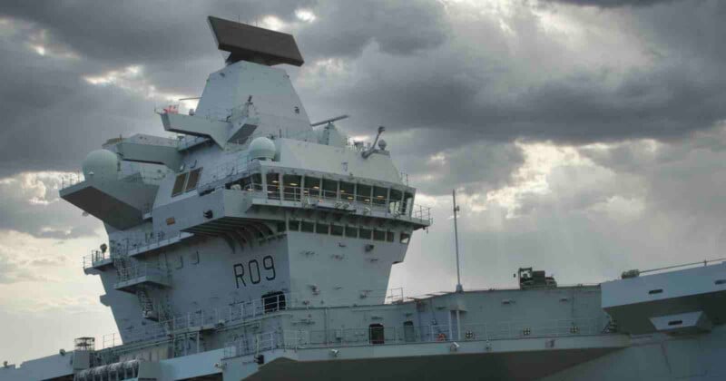 The island superstructure of a grey aircraft carrier marked with the pennant number R09 under a cloudy sky.