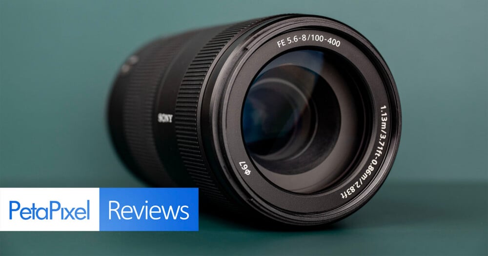 A black Sony camera lens sits on a dark green surface, with a PetaPixel Reviews logo in the bottom left corner.