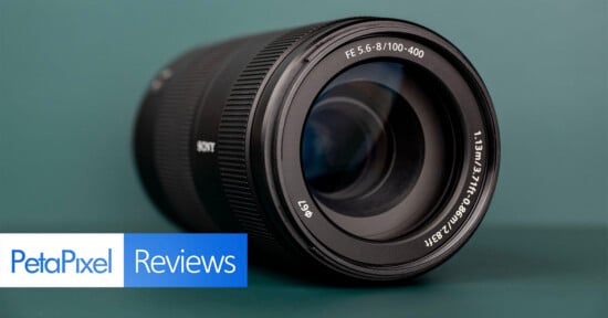 A black Sony camera lens sits on a dark green surface, with a PetaPixel Reviews logo in the bottom left corner.