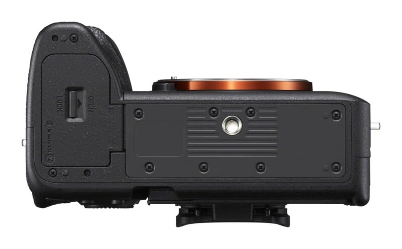 A bottom view of a black digital camera body, showing the battery compartment door, a tripod mount, and several small screws.