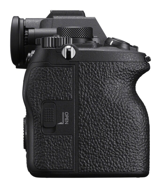 A side view of a black digital camera body showing the textured grip, a strap lug, a control dial, and a port cover labeled "OPEN.