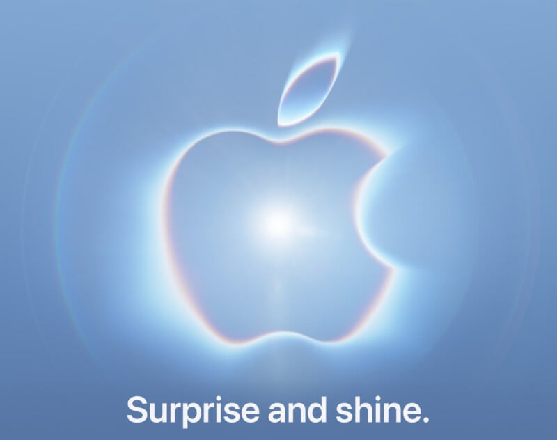 The Apple logo is centered against a light blue background, surrounded by a glowing, prismatic halo effect, with the text "Surprise and shine." below it.
