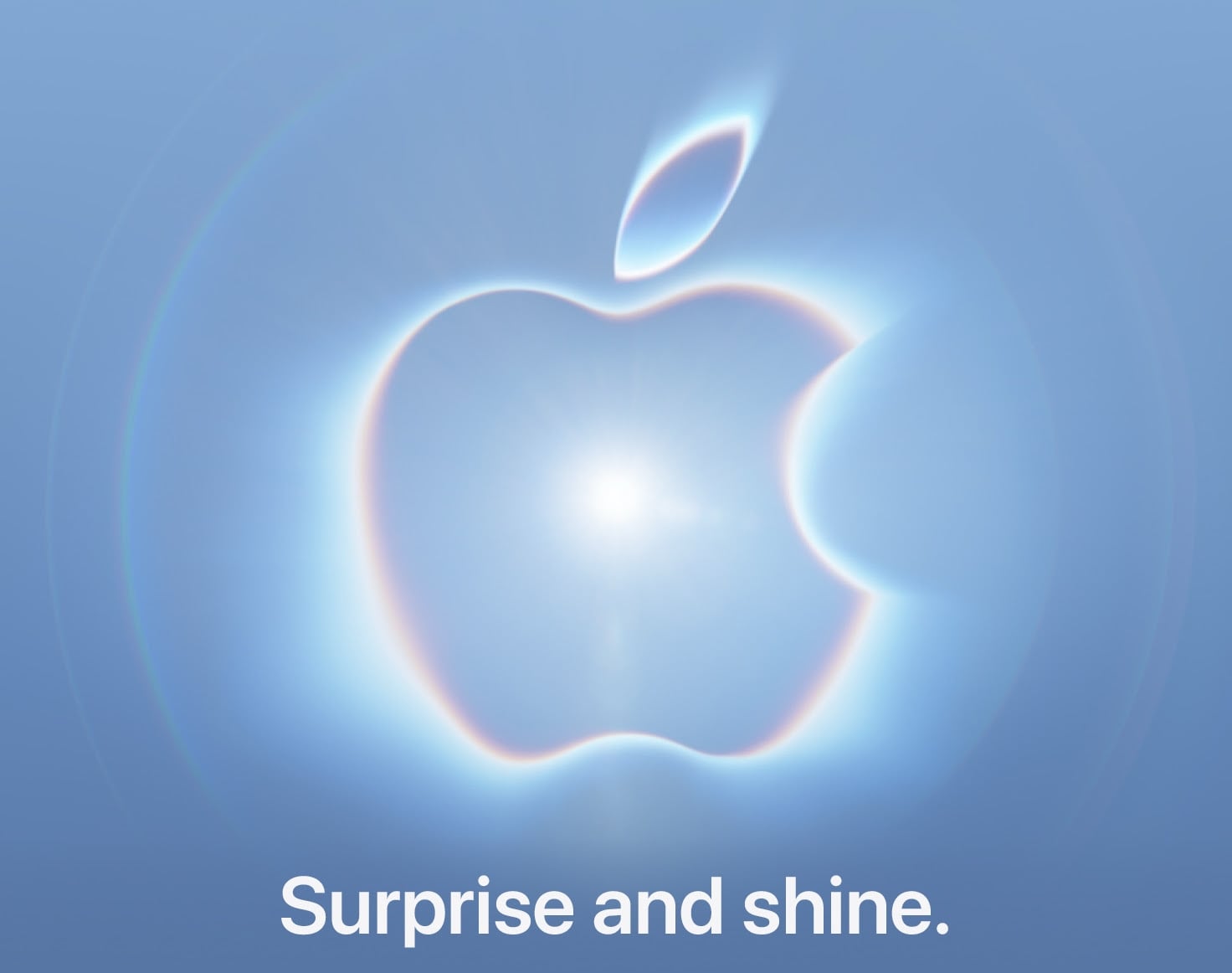 The Apple logo is centered against a light blue background, surrounded by a glowing, prismatic halo effect, with the text "Surprise and shine." below it.