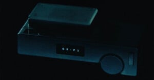 A dark, rectangular electronic device with a small screen displaying the text "G X - P 1" and a circular dial on the right side.