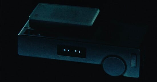 A dark, rectangular electronic device with a small screen displaying the text "G X - P 1" and a circular dial on the right side.