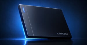 A black Samsung portable solid-state drive sits on a reflective surface against a dark blue background with a glowing blue light accent.