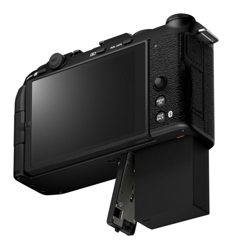 A black digital camera viewed from the back with its battery compartment door open and the battery partially extended.