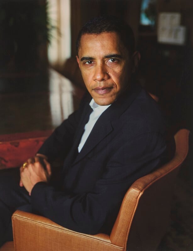 Barack Obama sits in a tan leather chair, wearing a dark suit jacket and white shirt, looking directly at the camera.