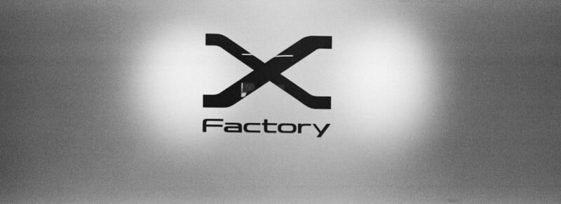 A black logo featuring a stylized letter X above the word "Factory" is centered on a frosted glass surface.