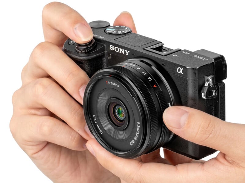 A pair of hands holds a black Sony a6400 mirrorless camera equipped with a 7Artisans 18mm F2.0 lens against a white background.