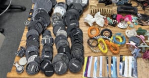A collection of camera lens caps, hair accessories, pacifiers, and plastic cards arranged on a wooden surface.