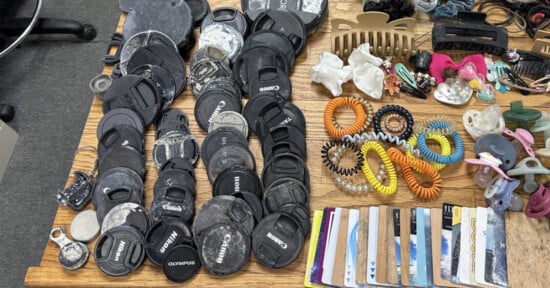A collection of camera lens caps, hair accessories, pacifiers, and plastic cards arranged on a wooden surface.