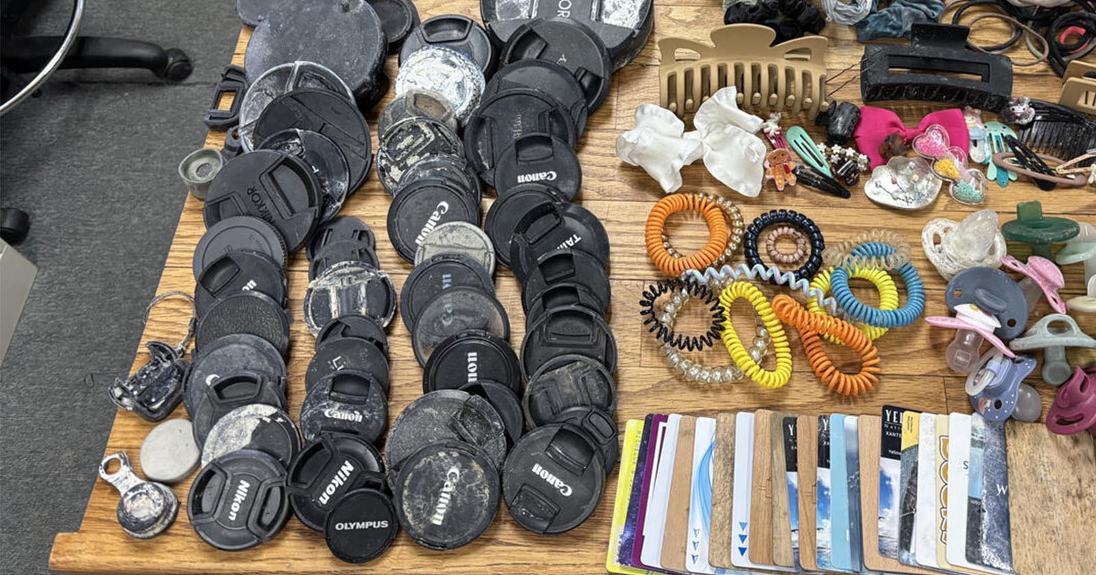 A collection of camera lens caps, hair accessories, pacifiers, and plastic cards arranged on a wooden surface.