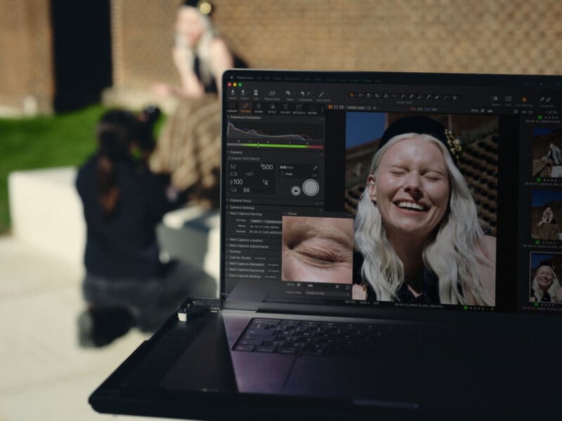 A laptop screen displays Capture One software showing a portrait of a smiling woman, with a photographer and subject visible in the blurred background.
