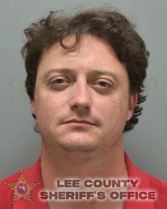 A mugshot of a man with wavy brown hair wearing a red shirt, with the Lee County Sheriff's Office logo in the corner.