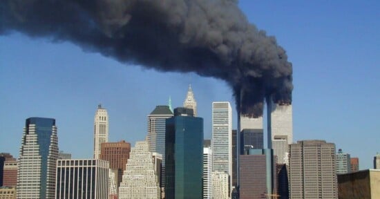 A view of the New York City skyline with thick black smoke billowing from the upper floors of the two World Trade Center towers.