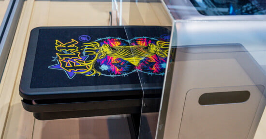 A t-shirt with a graphic of a yellow deer head and the word "ELK" sits on the tray of a garment printer.
