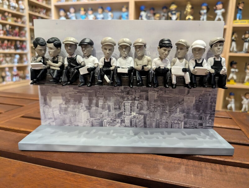 A bobblehead display featuring eleven figures sitting on a steel beam, modeled after the "Lunch Atop a Skyscraper" photograph.