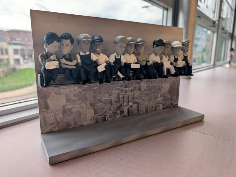 A 3D sculpture of eleven construction workers sitting on a beam, modeled after the iconic "Lunch atop a Skyscraper" photograph, displayed on a desk.