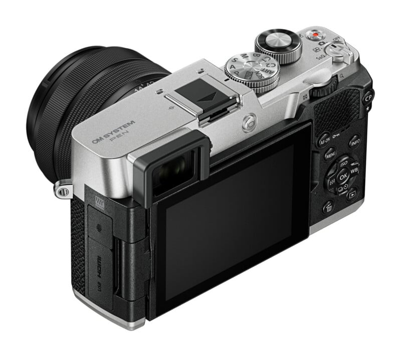 A silver and black mirrorless digital camera with an attached lens, viewed from the rear angle, showing the screen, buttons, and top dials.