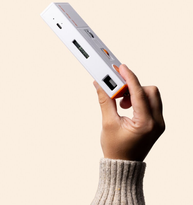 A hand wearing a beige knit sweater holds a white, rectangular portable power bank with orange accents and a small digital display.