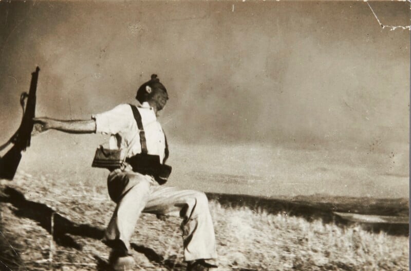 A sepia-toned photograph shows a soldier in a white shirt and suspenders falling backward on a grassy hillside while holding a rifle in his outstretched hand.