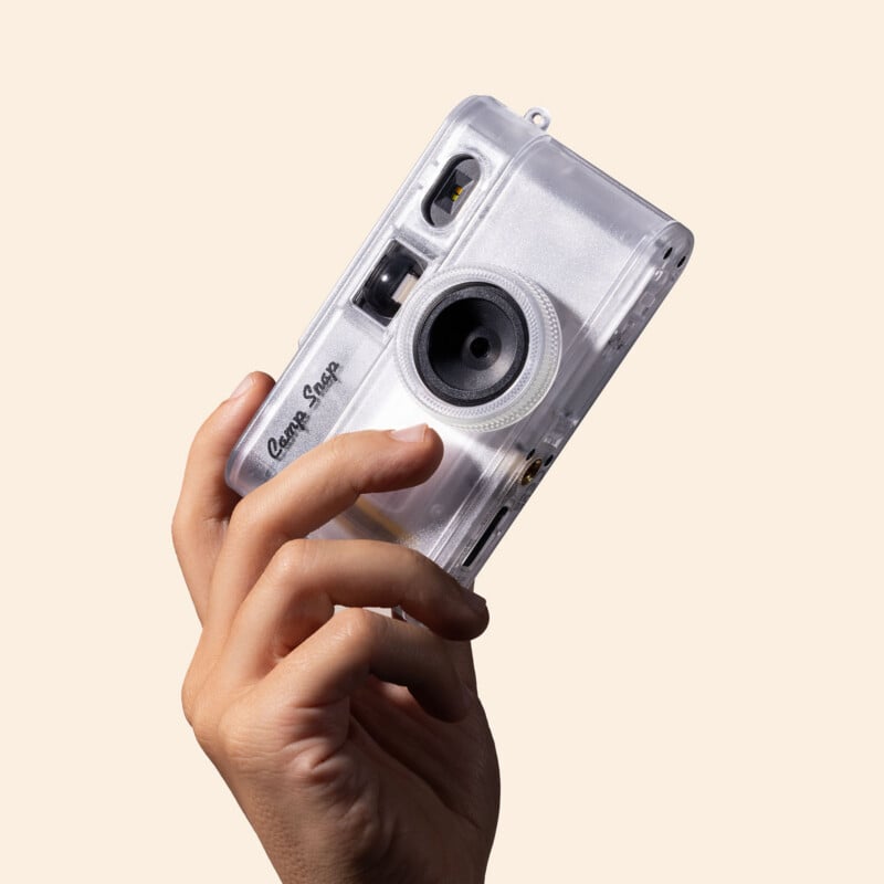A hand holds a clear, translucent digital camera with the text "Camp Snap" printed on the front.