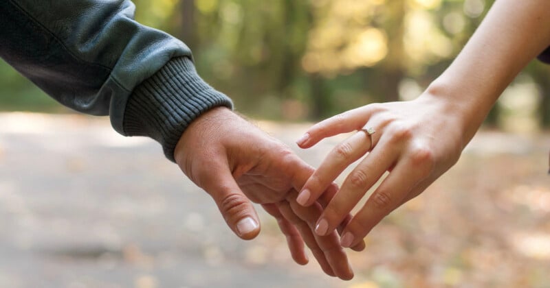 A close-up of two people reaching out to hold hands, with a diamond engagement ring visible on the woman's finger.