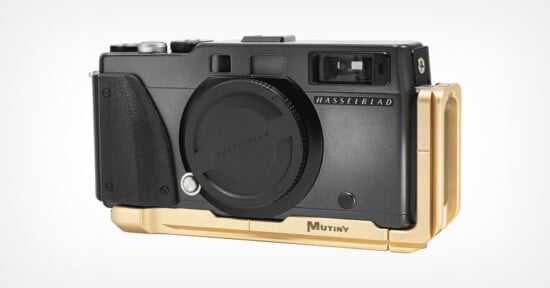 A black Hasselblad camera body with a lens cap attached, fitted with a gold-colored Mutiny metal base plate and side grip.