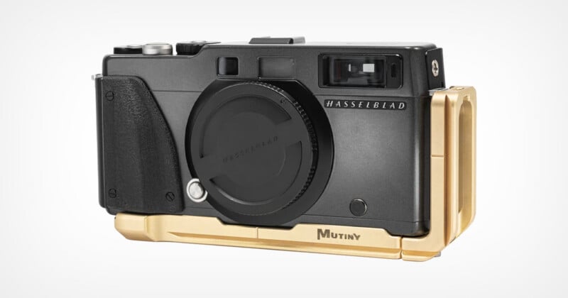 A black Hasselblad camera body with a lens cap attached, fitted with a gold-colored Mutiny metal base plate and side grip.