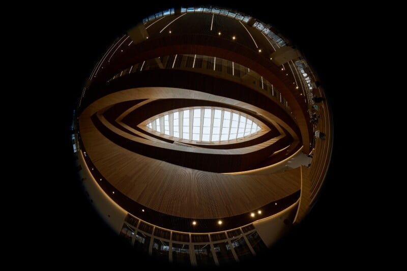 A fisheye view looking up at a multi-story atrium with curved wooden walls and a central oval skylight.