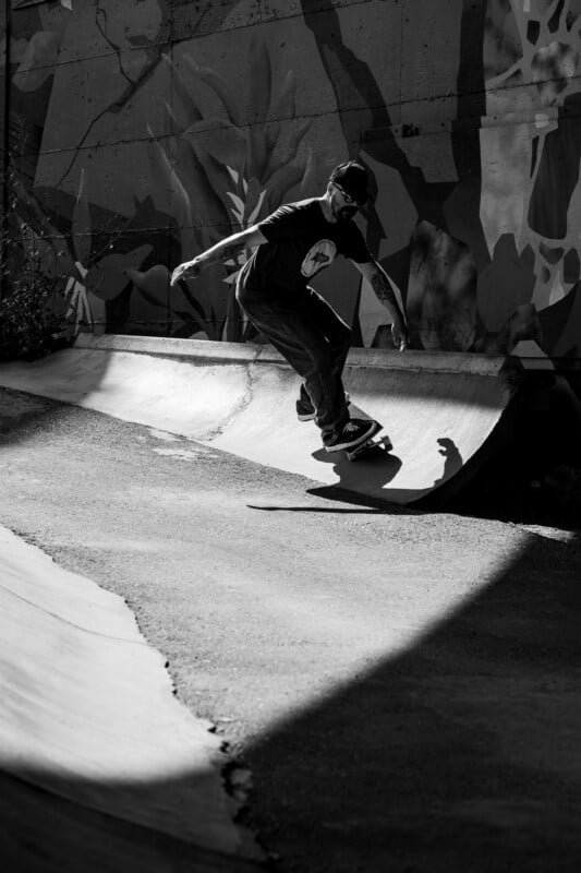 A man in a baseball cap and t-shirt skateboards along a concrete bank in front of a mural.