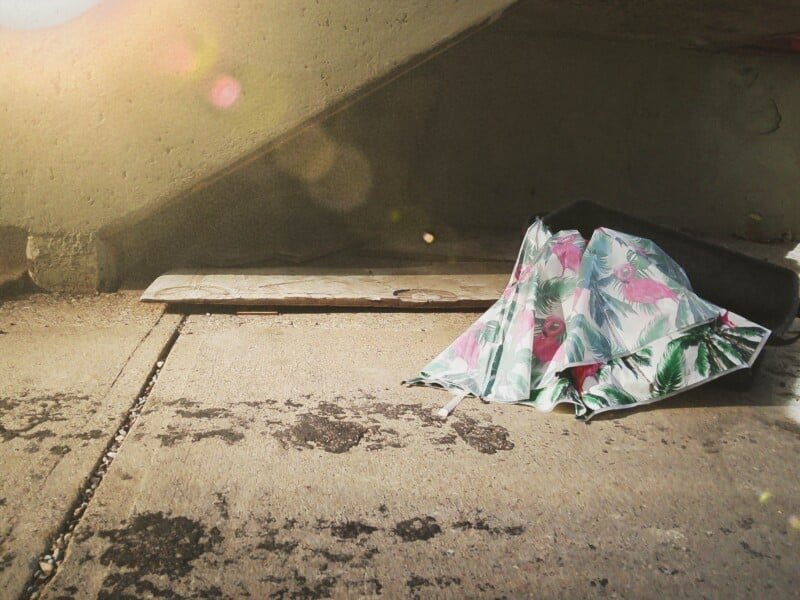A folded umbrella with a flamingo and palm leaf pattern rests on a concrete surface under a concrete overhang.