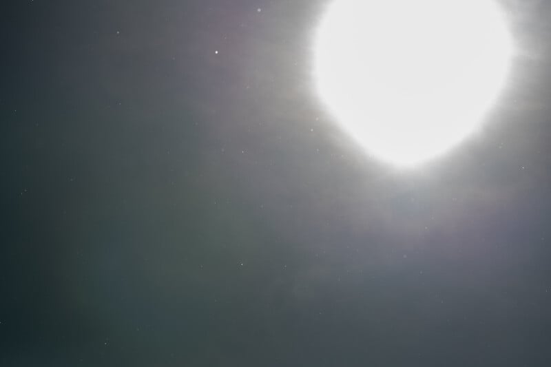 A bright, glowing sun shines in the upper right corner of a dark, hazy sky filled with scattered dust particles.