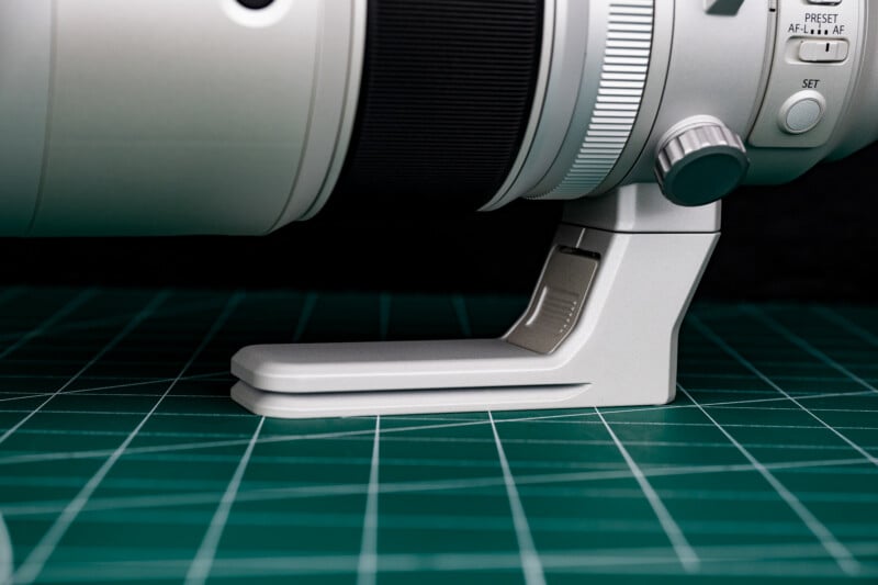 A close-up of a white camera lens tripod foot resting on a green cutting mat with white grid lines.