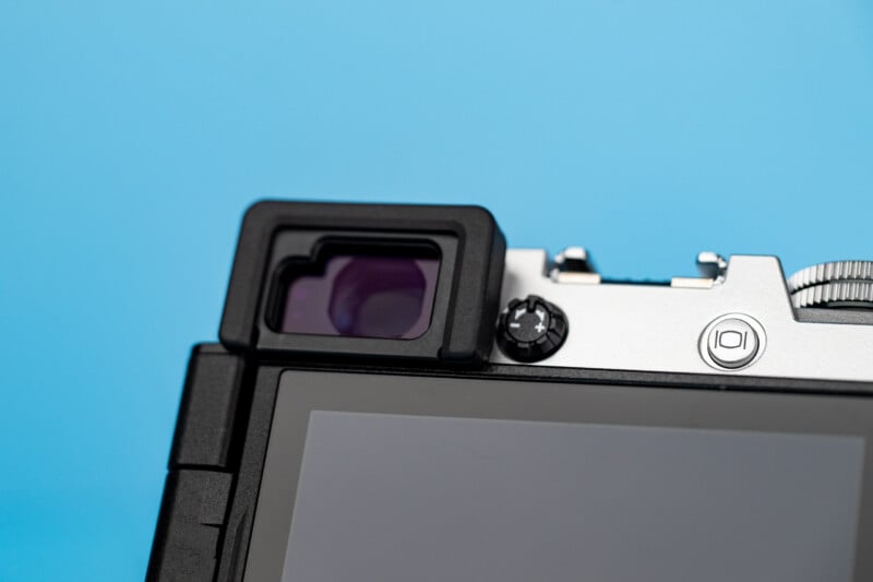 A close-up view of the back of a silver and black digital camera, showing the electronic viewfinder, a diopter adjustment dial, and a display screen against a solid blue background.