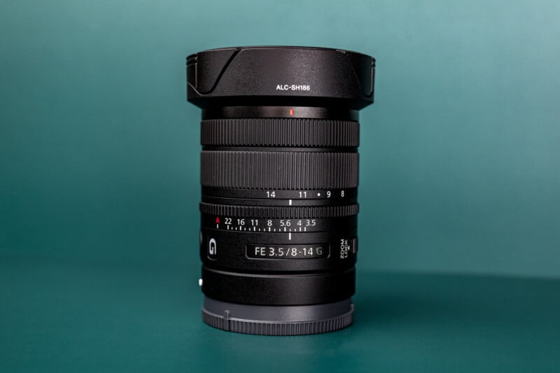 A black camera lens with a lens hood labeled ALC-SH186 stands upright against a solid teal background.