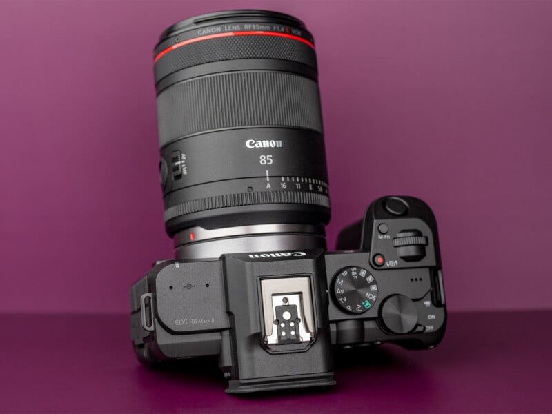 A Canon EOS R8 Mark II camera with a Canon RF 85mm lens attached, set against a solid purple background.