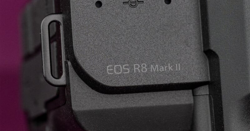 A close-up view of a black camera body with the text "EOS R8 Mark II" printed on the side, next to a metal strap lug.