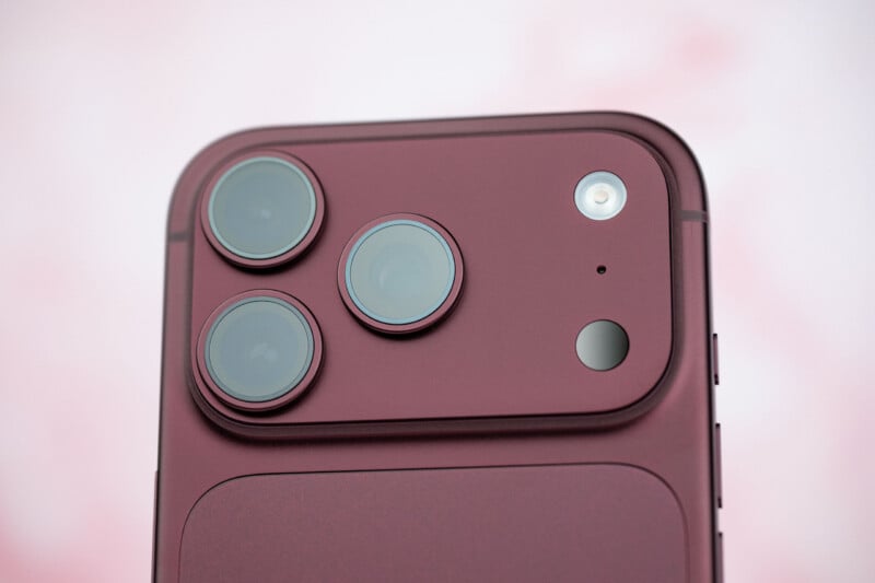 A close-up view of the back of a dark red smartphone, showing a triple-lens camera array, a flash, and a small sensor on a raised rectangular module.