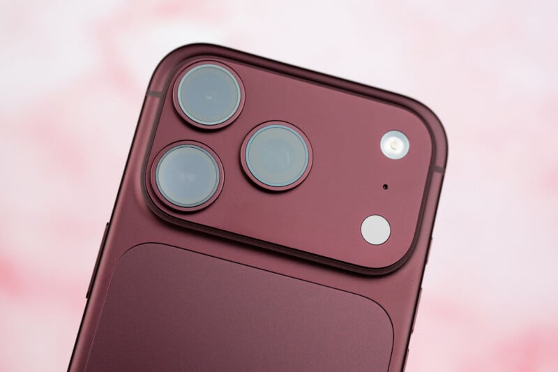 A close-up view of the back of a dark red smartphone, showing a triple-lens camera array, a flash, and a microphone set within a raised rectangular module.