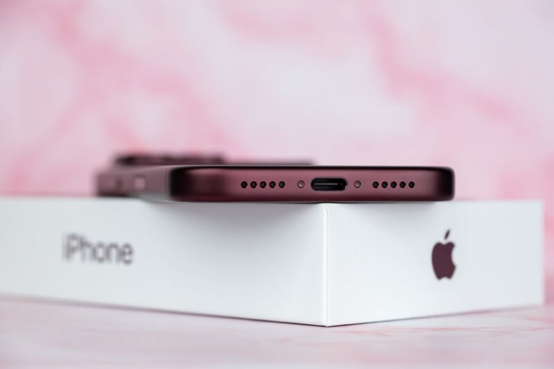 A dark red smartphone rests on top of a white iPhone box against a pink marble background.